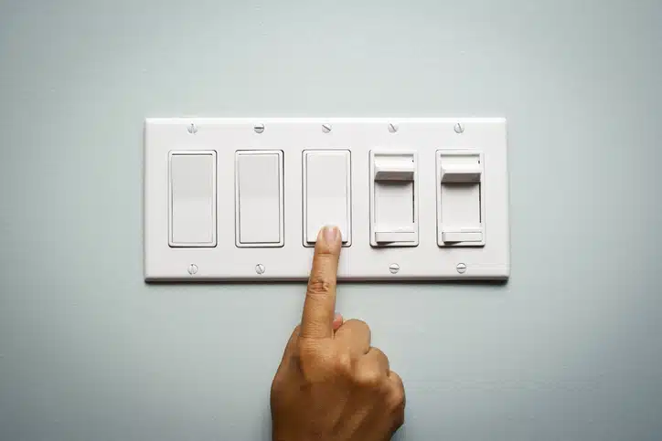 Woman's hand on a light switch showing that she is turning off the power and electricity to conserve energy